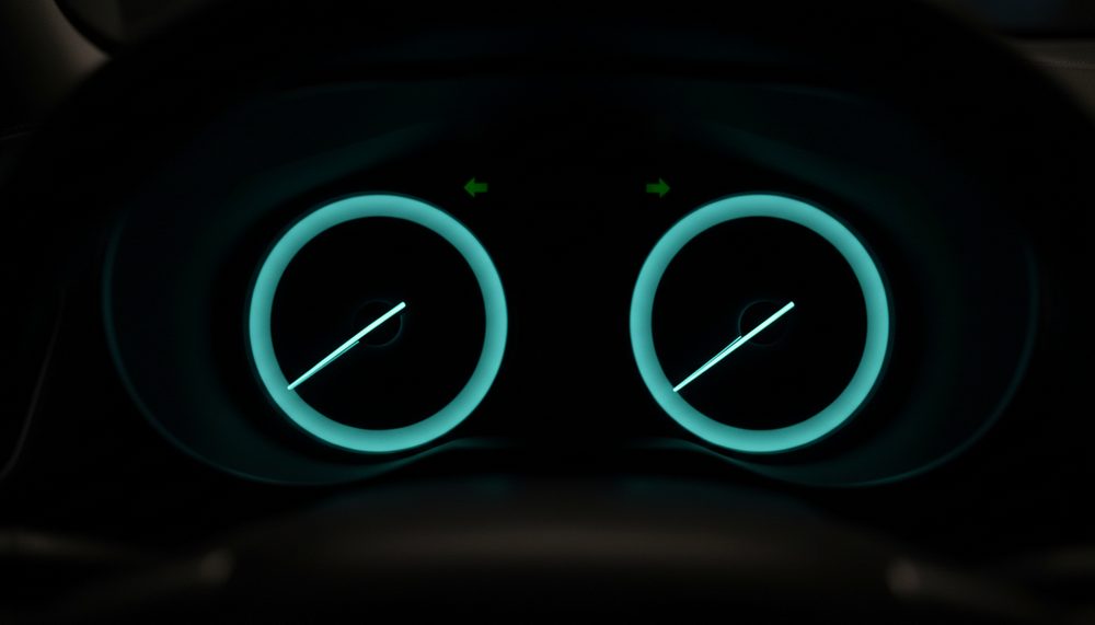 A car instrument cluster in a dark cabin with needles sweeping across unmarked dials.