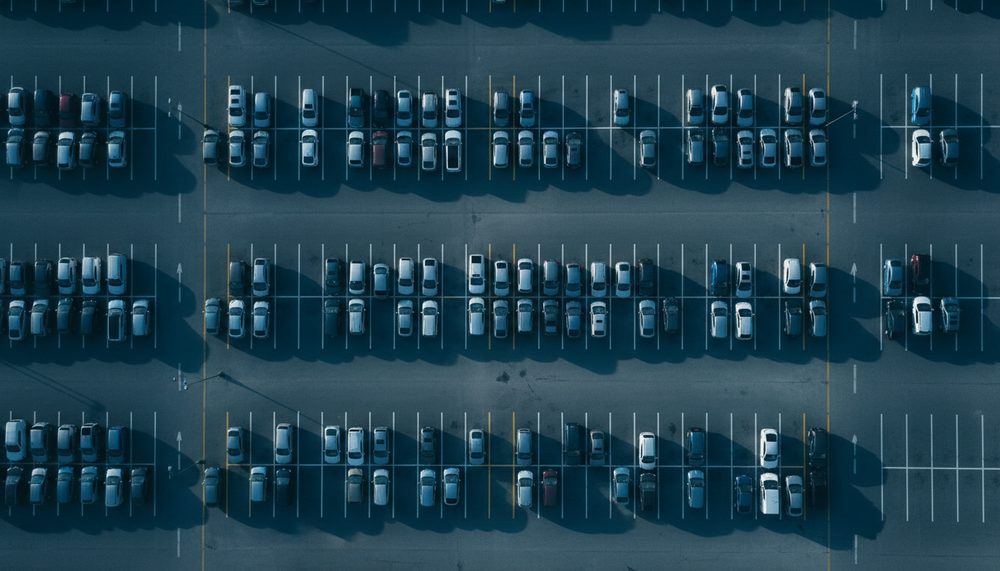 A half-full parking lot in orderly rows photographed from directly above in early morning light.